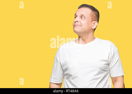 La mezza età uomo arabo wearig t-shirt bianco su sfondo isolato sorridente cercando lato e lo sguardo lontano pensando. Foto Stock