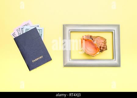 Concetto di vacanza estiva. Passaporto, denaro, photo frame, il Seashell giacciono su uno sfondo giallo Foto Stock