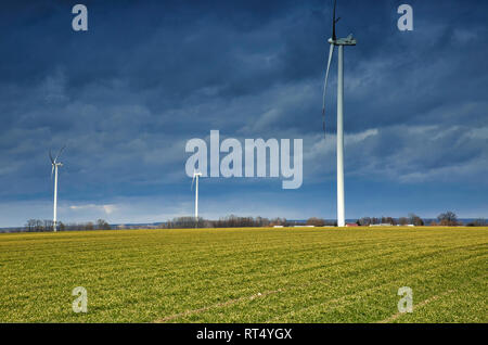 Tre mulini a vento per la produzione di energia elettrica è circondato da campi agricoli in polacco paese lato., contro lo sfondo della pesante, nuvole nere Foto Stock