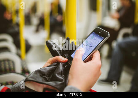 LONDON, Regno Unito - Mar 10, 2015: Donna utilizzando telefono dello smartphone all'interno metro stazione metropolitana con navigazione a mappa applicazione sulla schermata aperta e la ricerca per la prossima destinazione - Carro interno Foto Stock