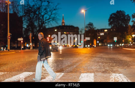 Strasburgo Francia - Ott 31 2017: Senior uomo attraversando via di notte davanti a vetture - rosso luce calda e chiara del cielo del Tramonto a Strasburgo, in Alsace Foto Stock