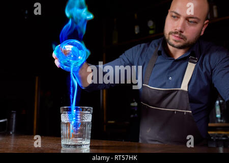 Fiery show presso il bar. Il barista fa caldo cocktail alcolico e infiamma bar. Il barman prepara un cocktail di Fiery. Fuoco su bar Foto Stock