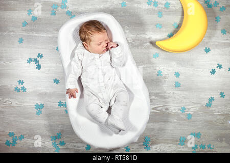 Il neonato dorme tranquillamente in una speciale materasso ortopedico Baby cocoon, su un pavimento di legno giocattolo luna e puzzle intorno a. La calma e il sonno sano nella nuova Foto Stock