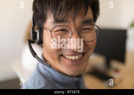 Executive maschio in cuffia sorridente in ufficio Foto Stock