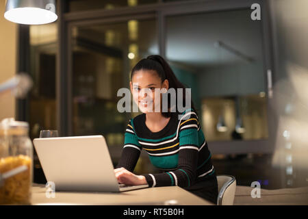 Ritratto di donna sorridente con notebook in appartamento a notte Foto Stock