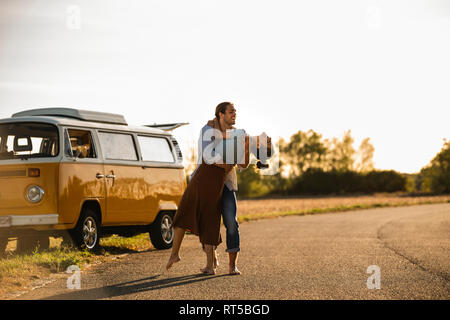 Coppia felice di fare un viaggio con un camper, ridendo e abbracciando sulla strada Foto Stock