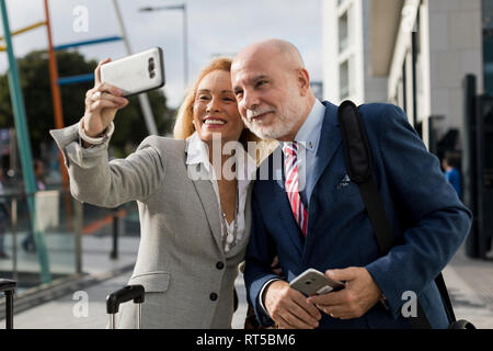 Imprenditore Senior e imprenditrice con bagaglio prendendo un selfie nella città Foto Stock