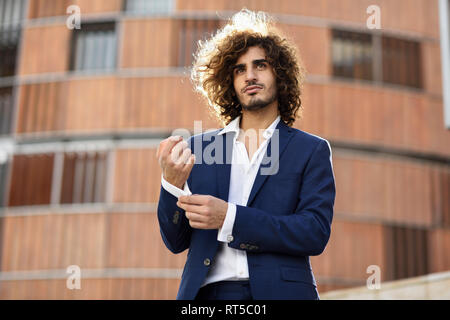 Ritratto di giovane imprenditore alla moda con capelli ricci indossare tuta blu abbottonatura cuff link Foto Stock