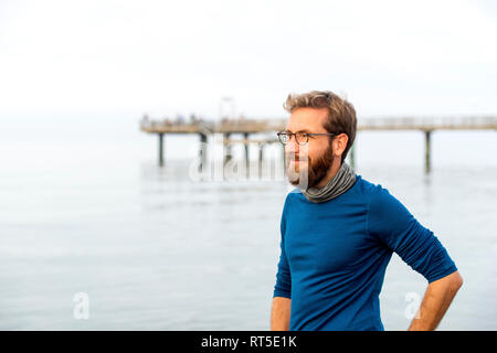 Germania, Rerik, uomo barbuto davanti al mare guardando a distanza sul giorno nebuloso Foto Stock