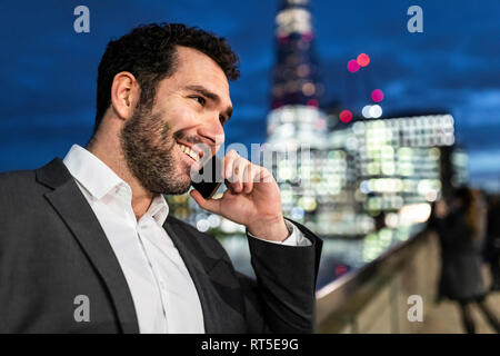 UK, Londra, ritratto di imprenditore sorridente parlando al telefono mentre il pendolarismo di notte Foto Stock