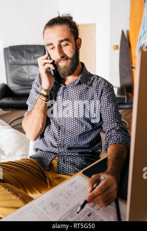 Giovani architetti che lavorano a casa con blueprint mentre si parla al telefono Foto Stock