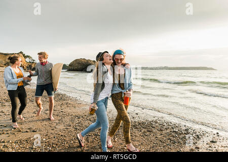 Happy amici con la tavola da surf e bevande camminando sulla spiaggia sassosa Foto Stock