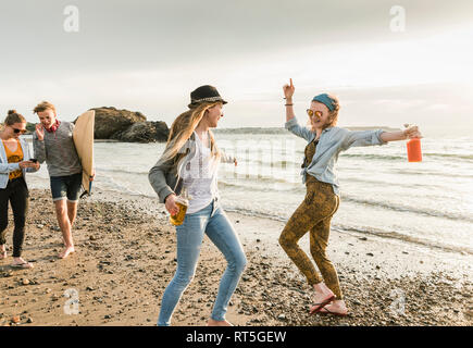 Happy amici con la tavola da surf e bevande camminando sulla spiaggia sassosa Foto Stock