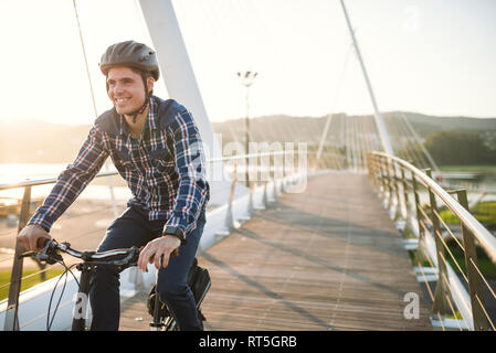 Giovane uomo Bicicletta Equitazione su un ponte al tramonto Foto Stock