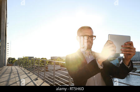 Imprenditore tenendo un selfie con tavoletta su un ponte della città Foto Stock