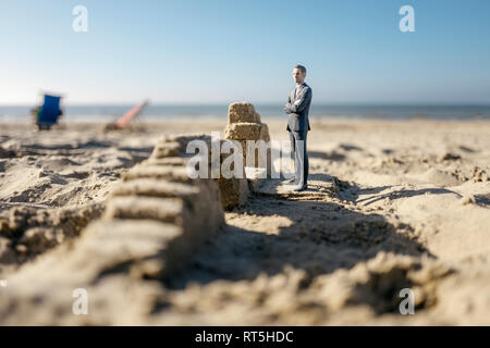 Imprenditore figurina permanente sulla sabbia da edifici di sabbia Foto Stock