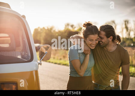 Affettuosa giovane di camminare sulla strada con bracci intorno, accanto al loro camper Foto Stock