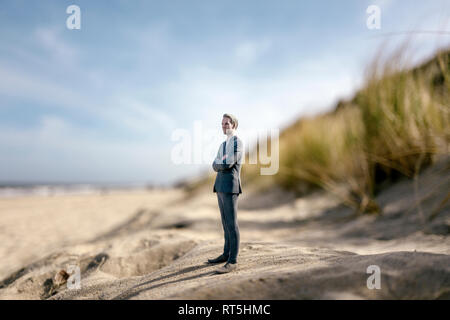 Imprenditore figurina permanente sulla duna di sabbia, guardando a distanza Foto Stock