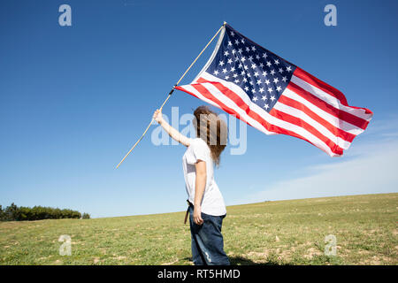 Ragazza con bandiera americana sul campo nel paesaggio remoto Foto Stock