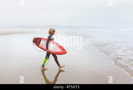 Spagna, Aviles, giovani surfer camminando verso l'acqua Foto Stock