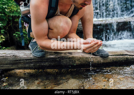 Giovane escursionista con zaino rinfrescante in acqua in una foresta, vista parziale Foto Stock