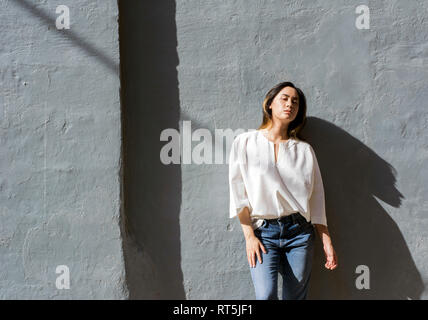 Ritratto di giovane donna appoggiata contro il muro grigio Foto Stock