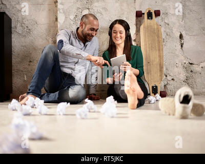 Sorridente colleghi seduti sul pavimento office sharing tablet Foto Stock