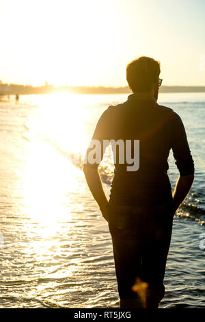 Silhouette di uomo, passeggiate sulla spiaggia al tramonto, vista posteriore Foto Stock