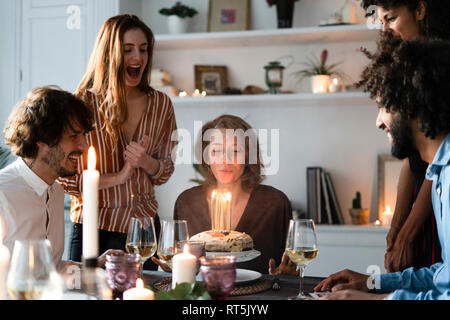 Amici sorprendente giovane donna con una torta di compleanno con candele accese Foto Stock