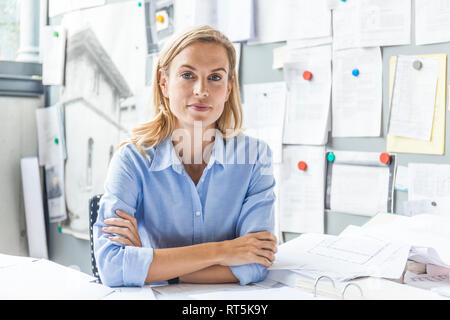 Ritratto di donna fiducioso seduto alla scrivania in ufficio circondato da documenti cartacei