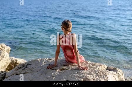 Croazia, Lokva Rogoznica, vista posteriore della ragazza seduta su di una roccia di fronte al mare