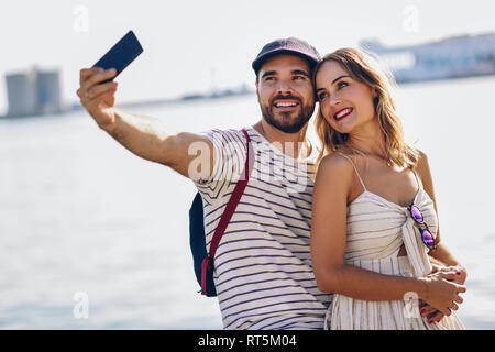 Spagna, Andalusia, Malaga, felice coppia turistica prendendo selfie con lo smartphone al litorale Foto Stock