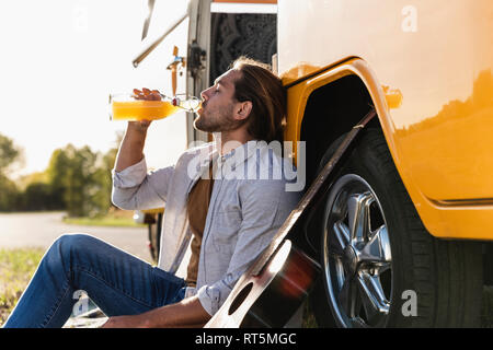 Giovane uomo su un viaggio con il suo camper, prendendo una pausa e di bere succo di frutta Foto Stock