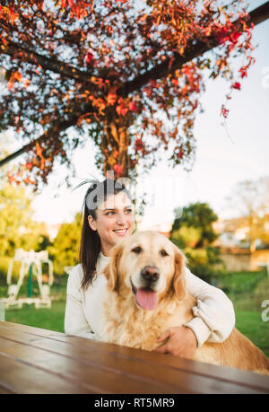 Sorridente giovane donna con il suo golden retriever cane di riposo in un parco Foto Stock