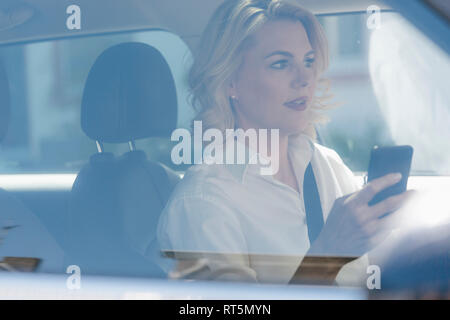 Imprenditrice utilizzando il telefono cellulare mentre si guida auto Foto Stock