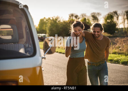 Affettuosa giovane di camminare sulla strada con bracci intorno, accanto al loro camper Foto Stock