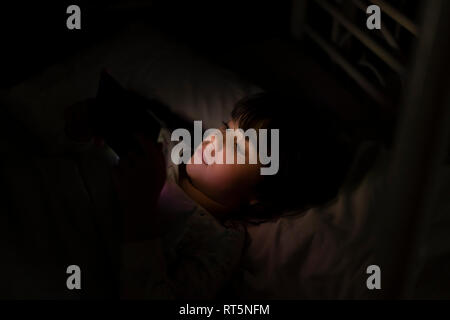Ragazza distesa nel letto utilizza lo smartphone durante la notte Foto Stock
