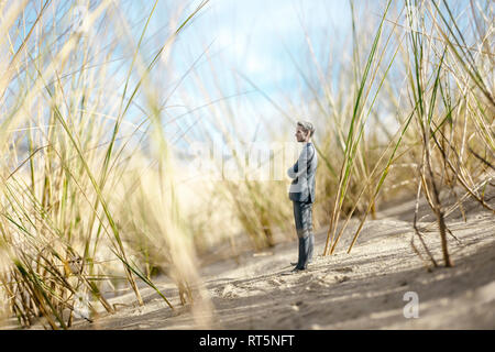 Imprenditore figurina permanente sulla duna di sabbia, guardando a distanza Foto Stock