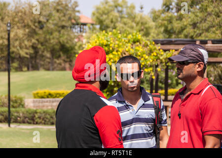 Un trio di indiani gli uomini impegnati in una conversazione su un luminoso giorno d'estate. Uno degli uomini è alla ricerca e sorridente alla fotocamera. Unità nella diversità. Foto Stock