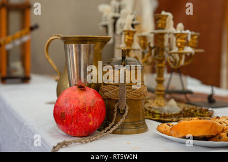 Un rosso frutto di melograno, metallo vintage boccale di birra, un bicchiere di vino e una brocca. Alcune torte fatte in casa sul tavolo, candelabri in background Foto Stock