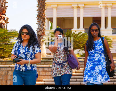 Un trio di smart, fiducioso, belle donne indiane indossando floral tops, tenendo le telecamere e scattare foto e a piedi giù per una rampa di scale. Foto Stock