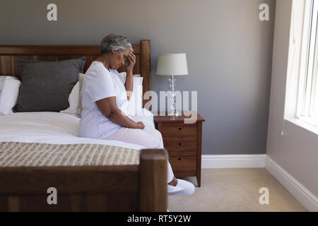 Preoccupato senior donna seduta su di un letto di casa Foto Stock
