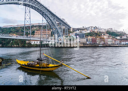 Porto, Portogallo - Dicembre 2018: Giallo Rabelo barca il trasporto di vino di Porto, nel fiume Douro con Luis I ponte dietro. Foto Stock