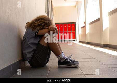 Triste schoolgirl seduta sul pavimento con la sua testa in basso Foto Stock