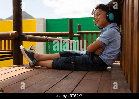 Schoolgirl ascoltando musica sulle cuffie nella scuola parco giochi Foto Stock