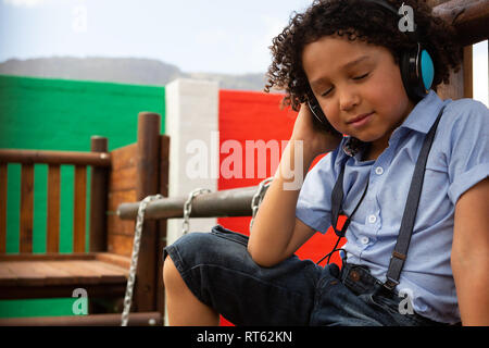 Schoolgirl ascoltando musica sulle cuffie nella scuola parco giochi Foto Stock