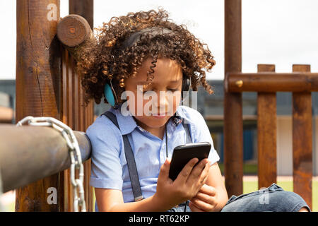 Schoolgirl utilizzando il telefono cellulare nella scuola parco giochi Foto Stock