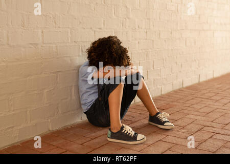 Triste schoolgirl seduto da solo sul pavimento nel corridoio Foto Stock