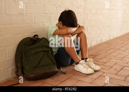 Triste schoolboy seduto da solo sul pavimento nel corridoio Foto Stock