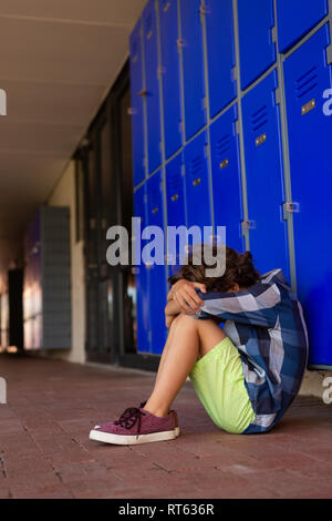 Triste schoolboy seduto da solo sul pavimento nel corridoio Foto Stock